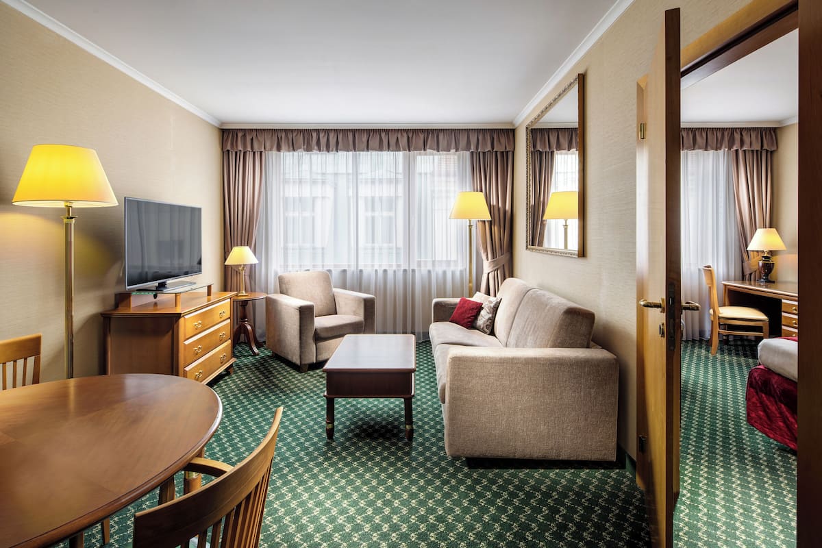 Een hotelkamer met een bank, fauteuil, eettafel en een televisie.