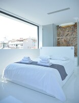 Quarto de hotel moderno com uma cama grande, toalhas dobradas com cuidado e vista para a cidade através de uma grande janela.