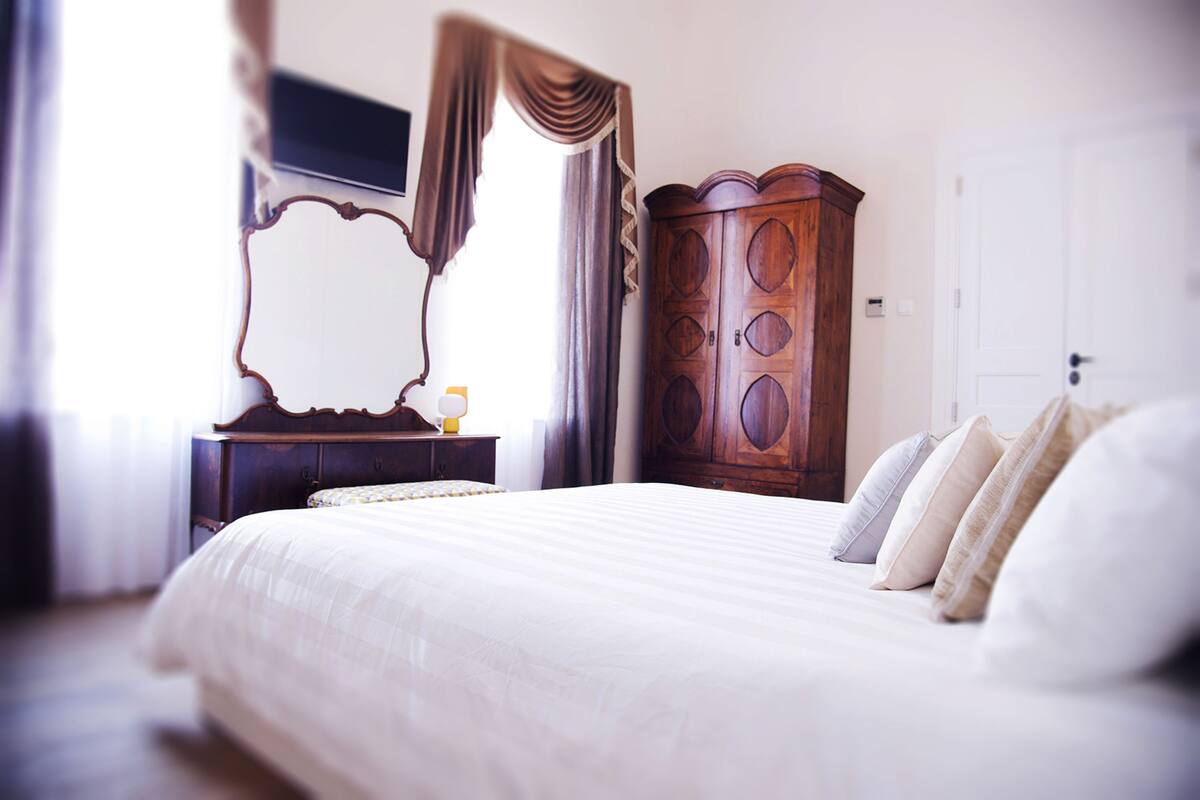 A neatly made bed with a large mirror and a wooden wardrobe in a well-lit room.