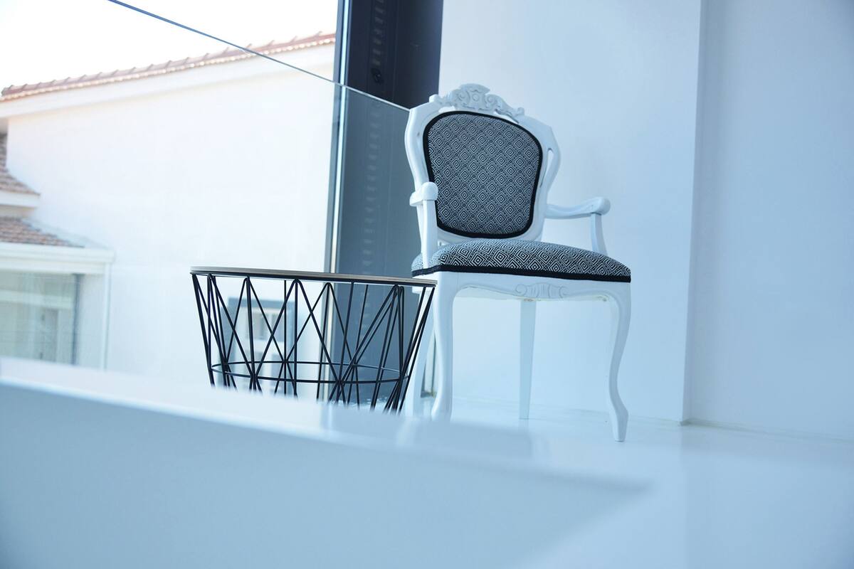 A white chair with a patterned cushion on a balcony with a metal basket.