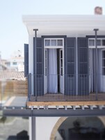 Un modelo de un edificio con balcón, una puerta con contraventanas y una ventana con cortinas.