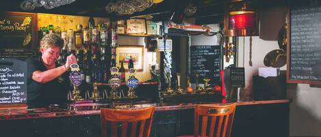 A bar with a bartender pouring a drink, shelves of liquor bottles, and a chalkboard menu.