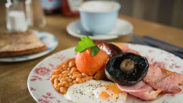A plate of breakfast food including eggs, bacon, beans, and a tomato.