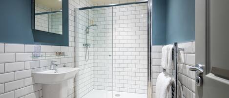 Un baño moderno con ducha separada por mampara de cristal, azulejos blancos, un lavabo y un espejo.