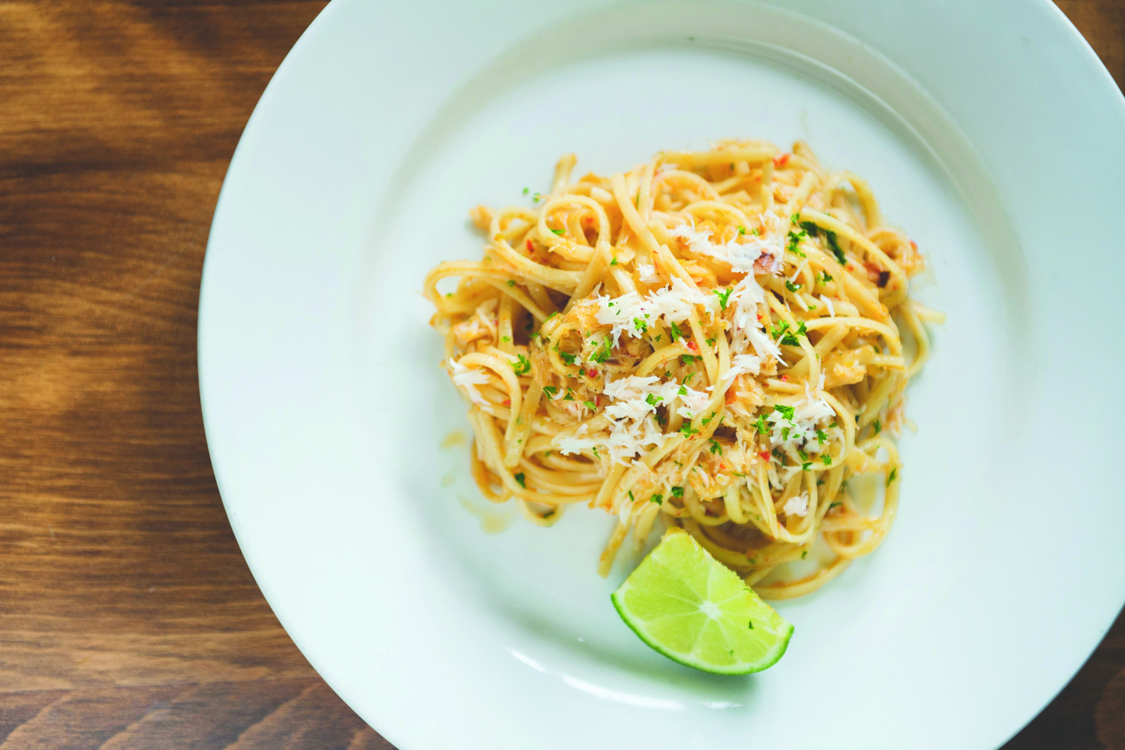 A plate of spaghetti with grated cheese and a lime wedge on a white plate.