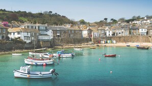 Une ville côtière où des bateaux sont amarrés dans un port, avec des bâtiments en pierre et une plage de sable.