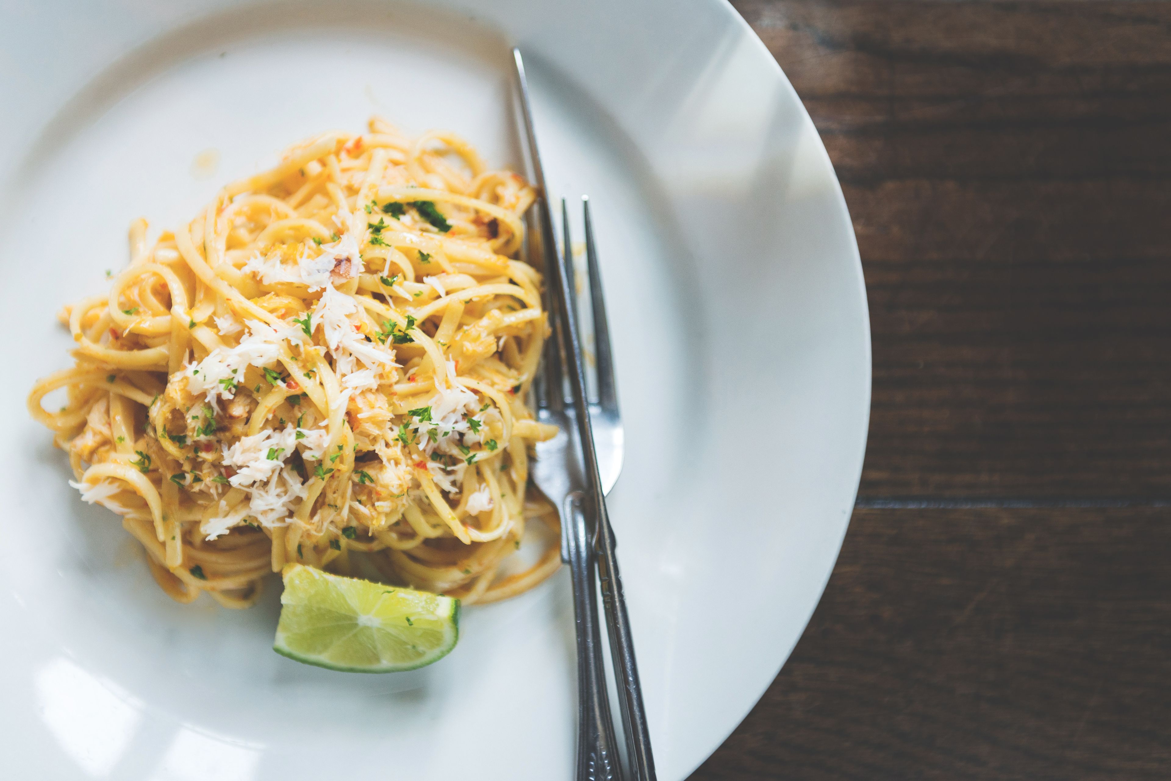 Eine Portion Spaghetti mit Kräutern und geriebenem Käse, dazu ein Limettenschnitz.