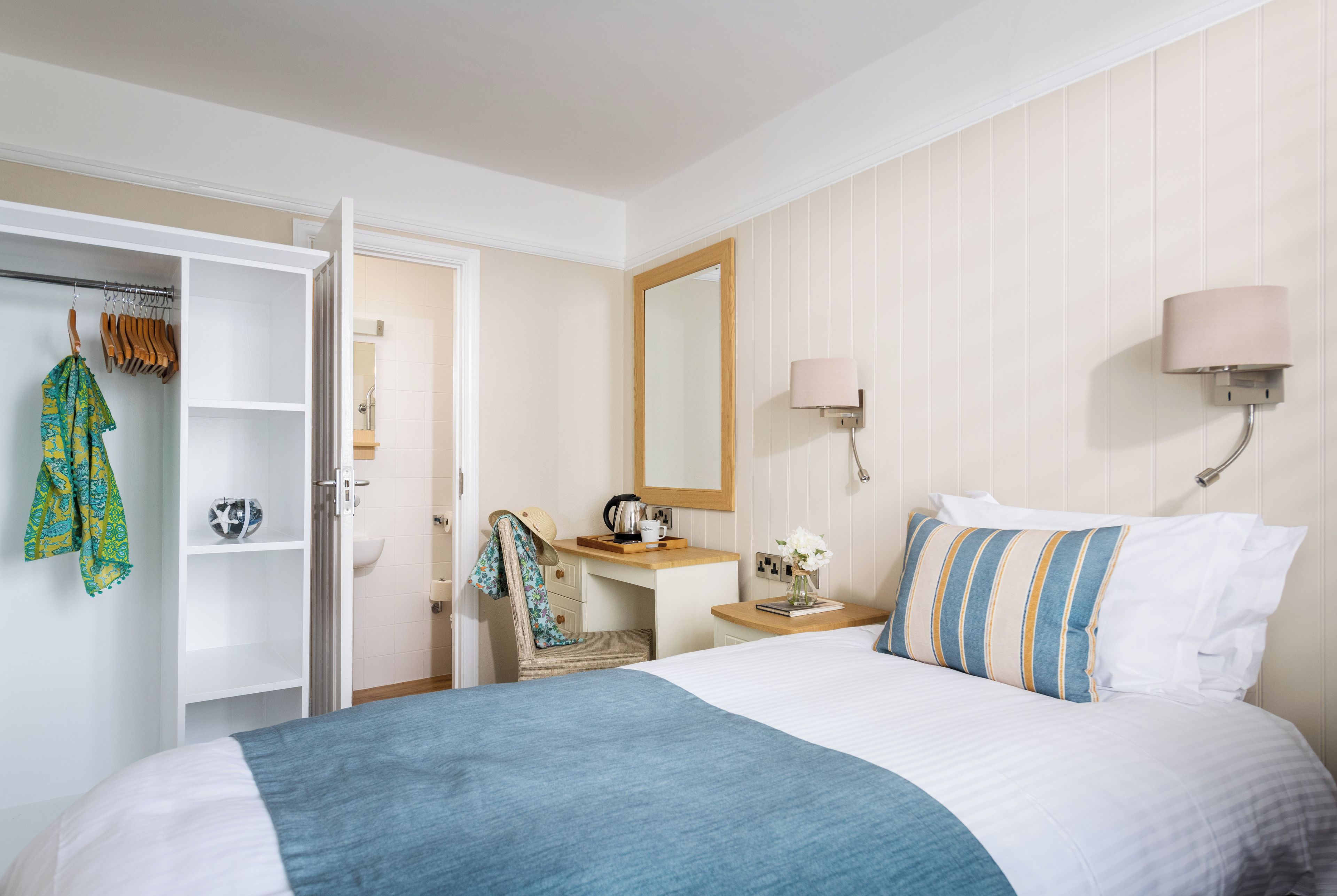 A hotel room with a bed, a desk with a mirror, a wardrobe, and a bathroom.
