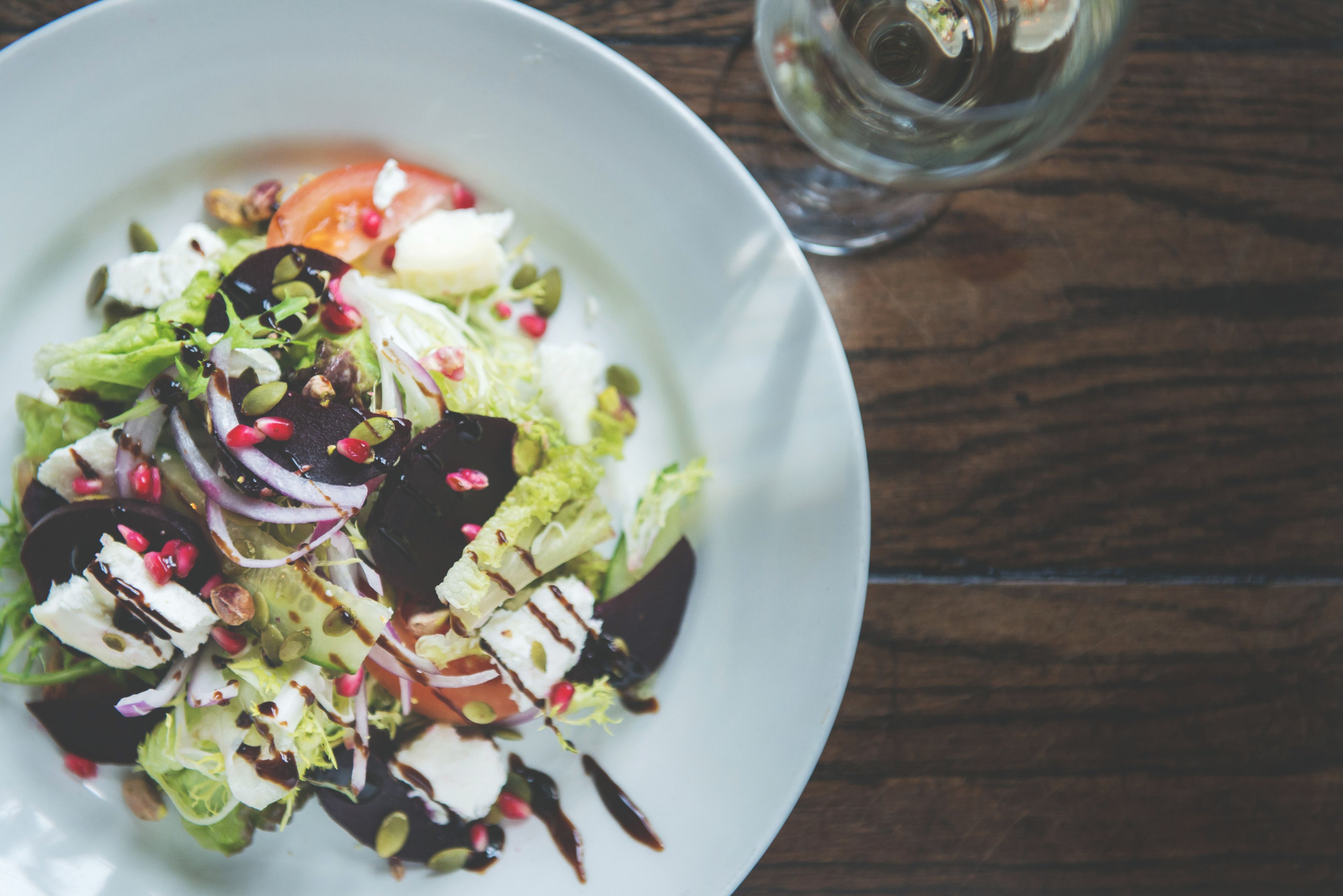 A white plate with a salad on a wooden table.