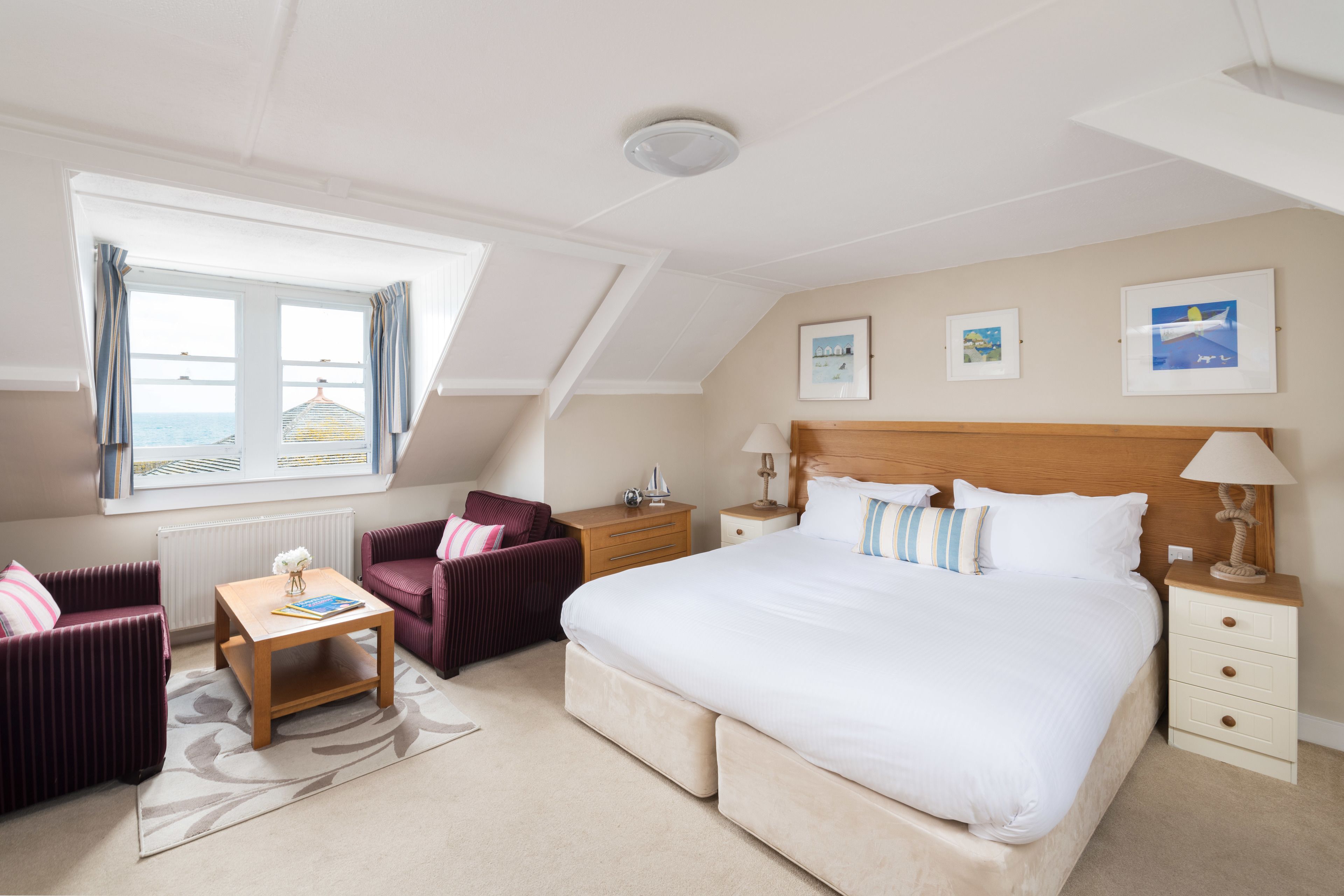 A bedroom with a large bed, a nightstand, a bedside table, a chair, a small table, and a window with curtains.