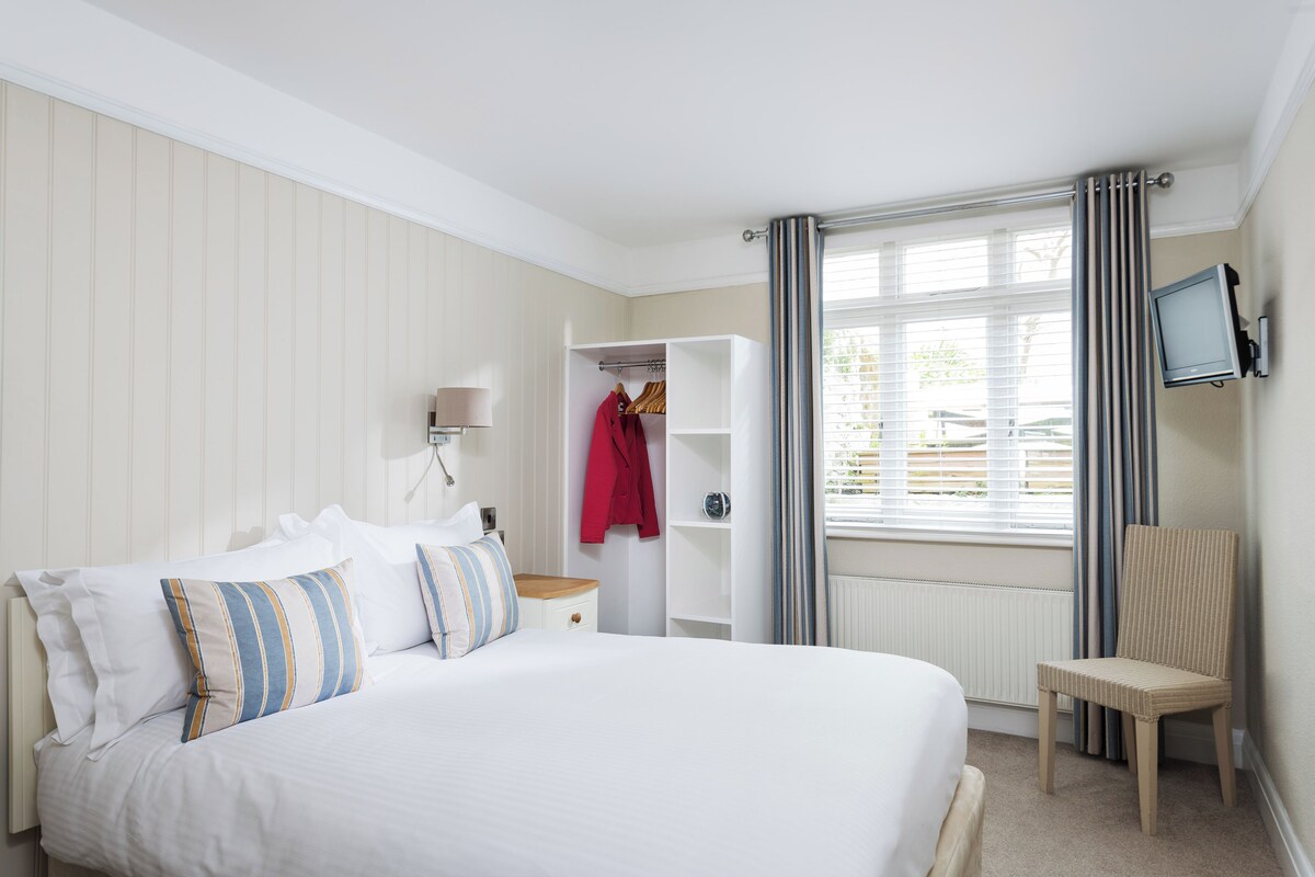 Une chambre d’hôtel avec un grand lit, une armoire, une chaise et un téléviseur fixé au mur.
