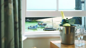 Une vue par la fenêtre sur des bateaux amarrés à un quai, une bouteille de champagne et un verre posés sur une table en bois.