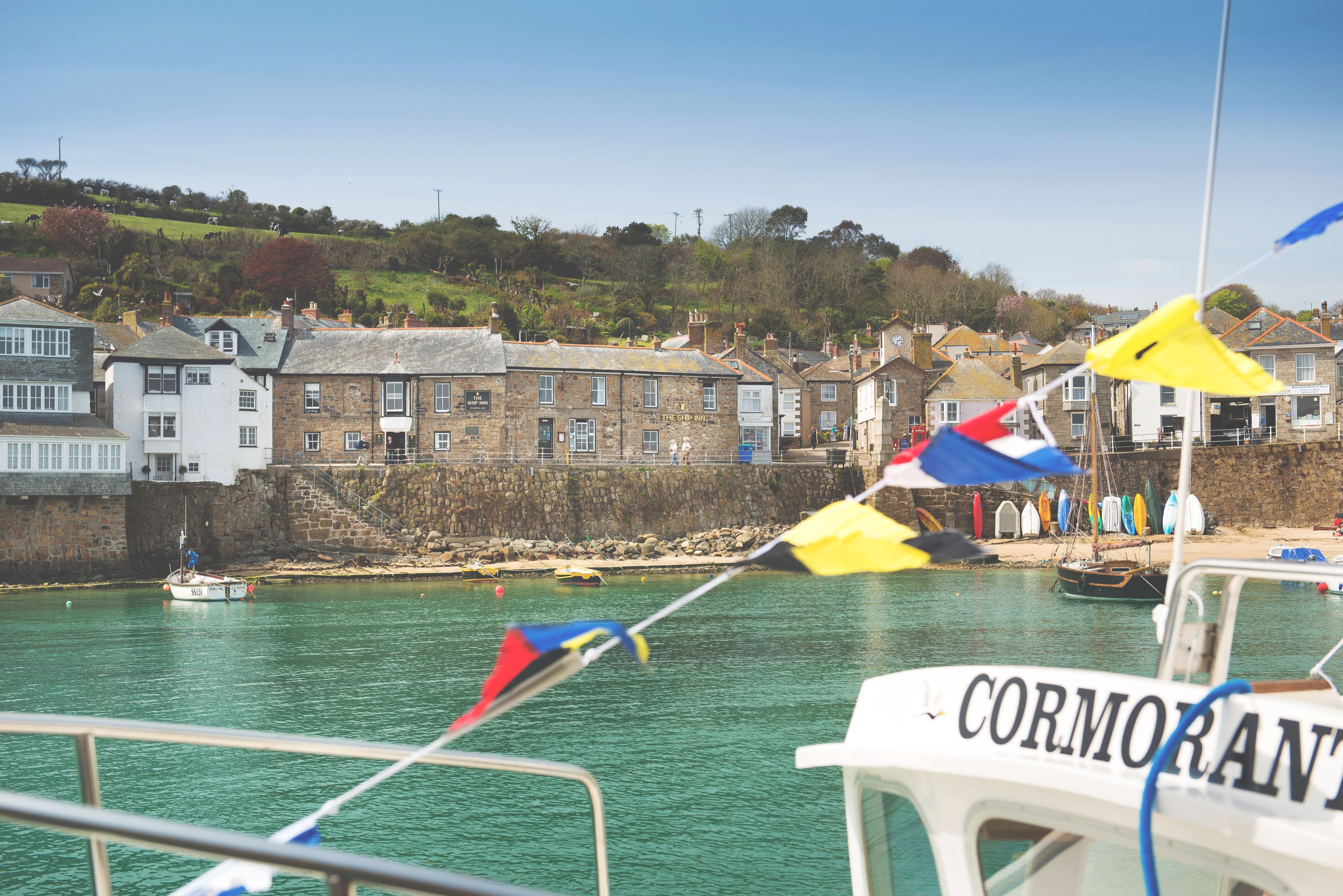 Une ville côtière avec des bâtiments en pierre, un port et un bateau appelé « CORMORAN ».