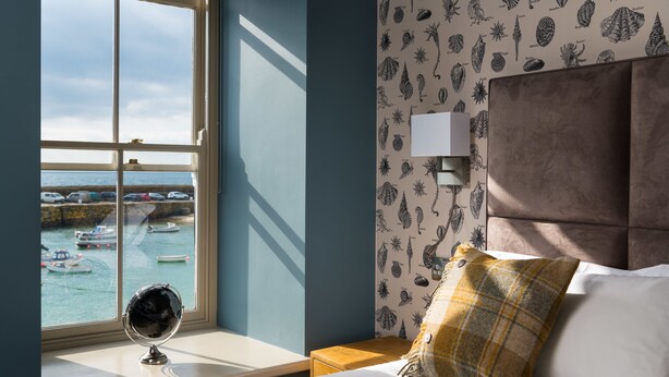 Une chambre avec vue sur les bateaux qui naviguent, visible par la fenêtre, un globe posé sur le rebord de la fenêtre et une tête de lit dotée d’un luminaire.