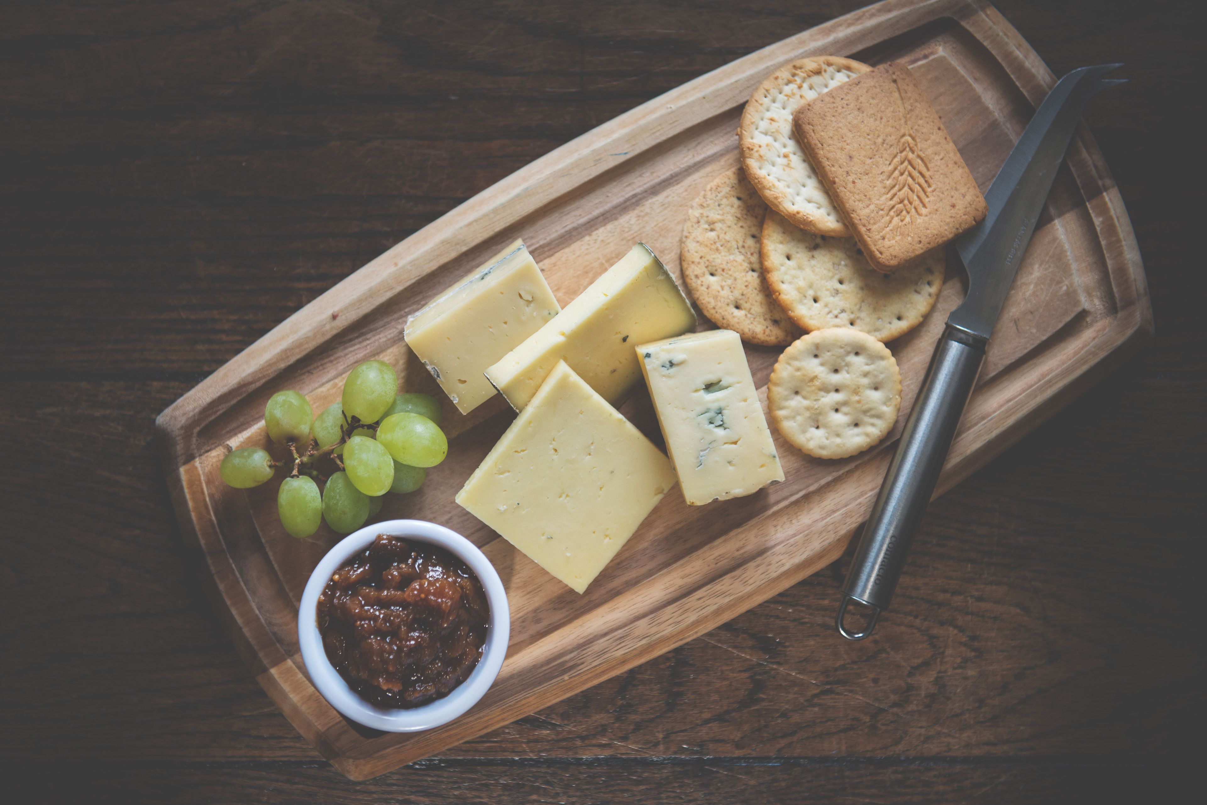 Una tabla de madera con queso, galletas, uvas y un cuchillo.
