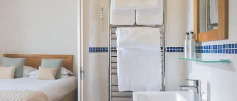 Una habitación de hotel con cama, baño con lavamanos y espejo, y un perchero para toallas.