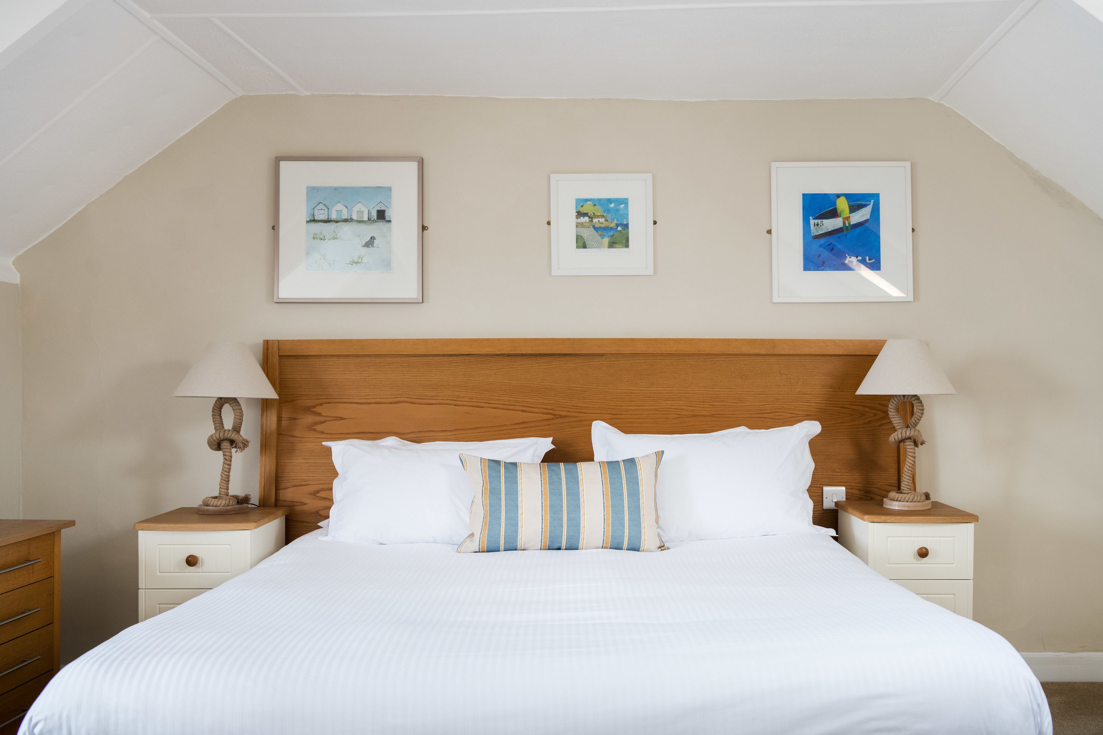 A neatly made bed with white bedding, two nightstands with lamps, and three framed pictures on the wall.