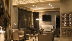A modern living room with a high ceiling, a flat-screen TV mounted on the wall, and a decorative ceiling panel. - Queen's Hotel (Skopje)