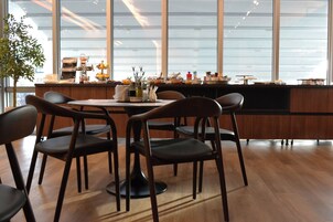 Un comedor moderno con una mesa y sillas de madera, una barra con diversos objetos, y ventanas amplias que aportan luz natural.