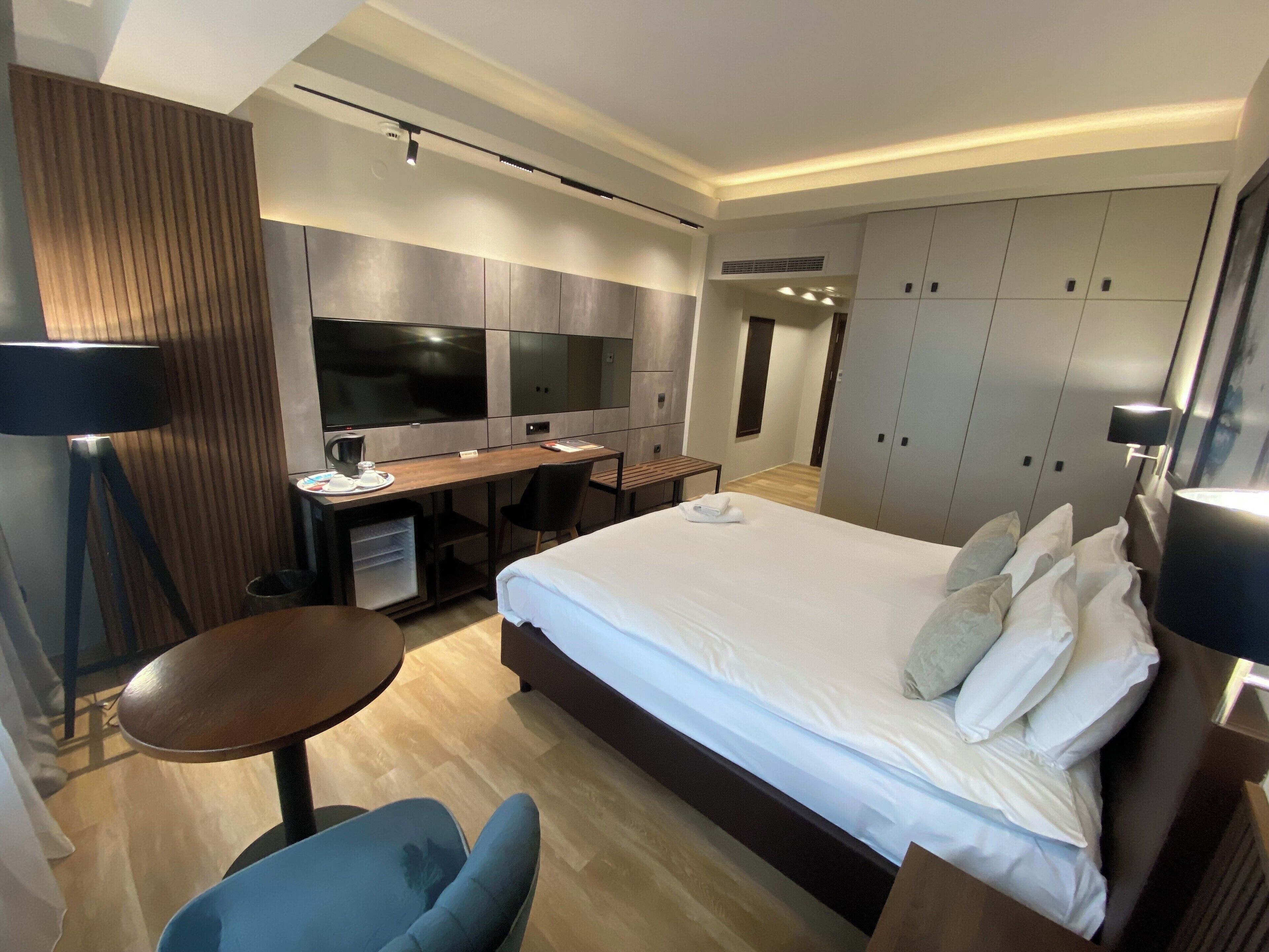 Une chambre d’hôtel moderne dotée d’un grand lit, d’un bureau avec un téléviseur à écran plat, d’un coin salon avec un fauteuil et d’une armoire.