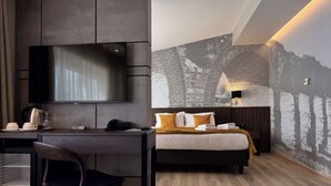 A modern hotel room with a flat-screen TV, a desk with a telephone, and a bed with a patterned wall behind it. - Queen's Hotel (Skopje)
