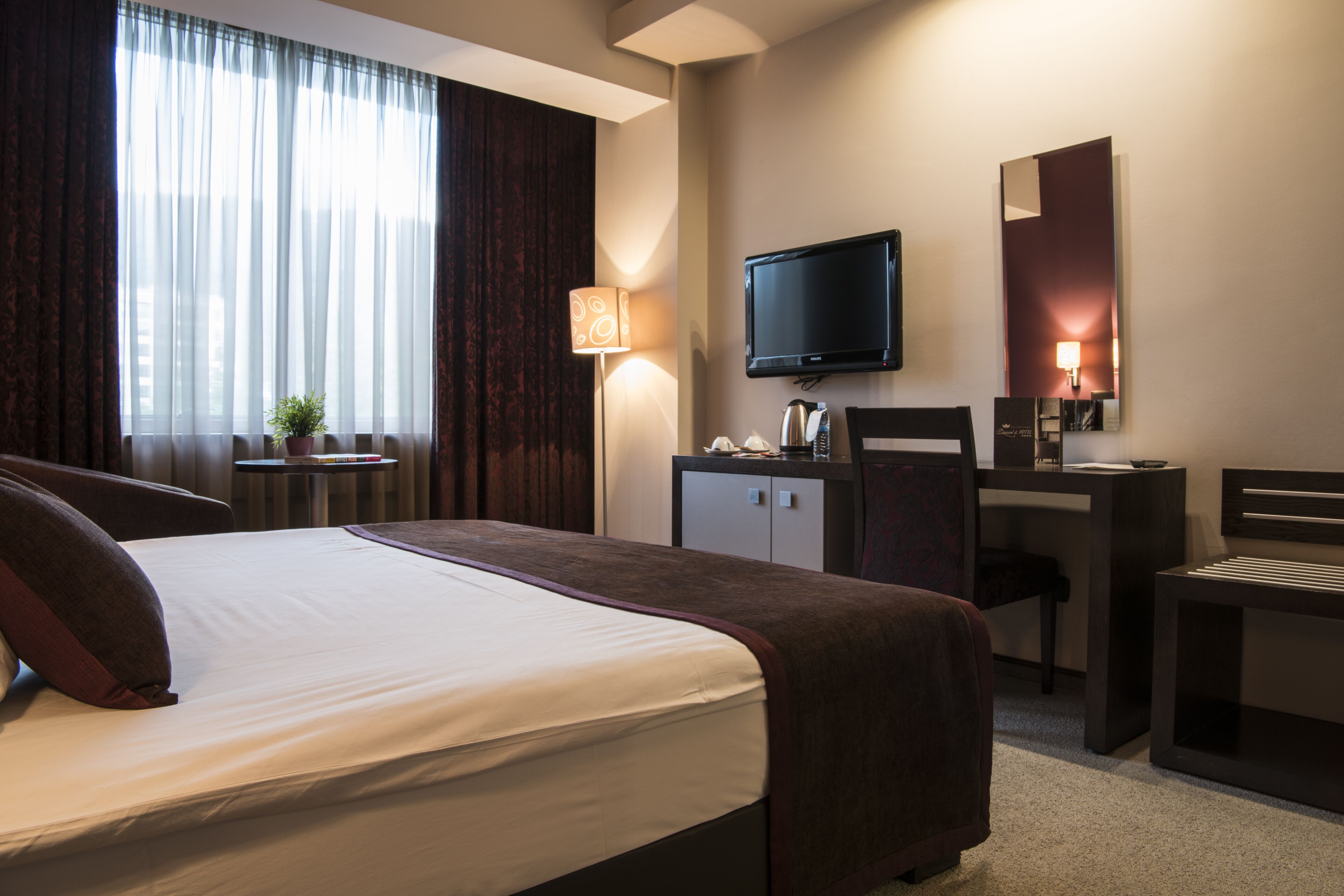 Una habitación de hotel con una cama, un escritorio, una silla, un televisor y un espejo.
