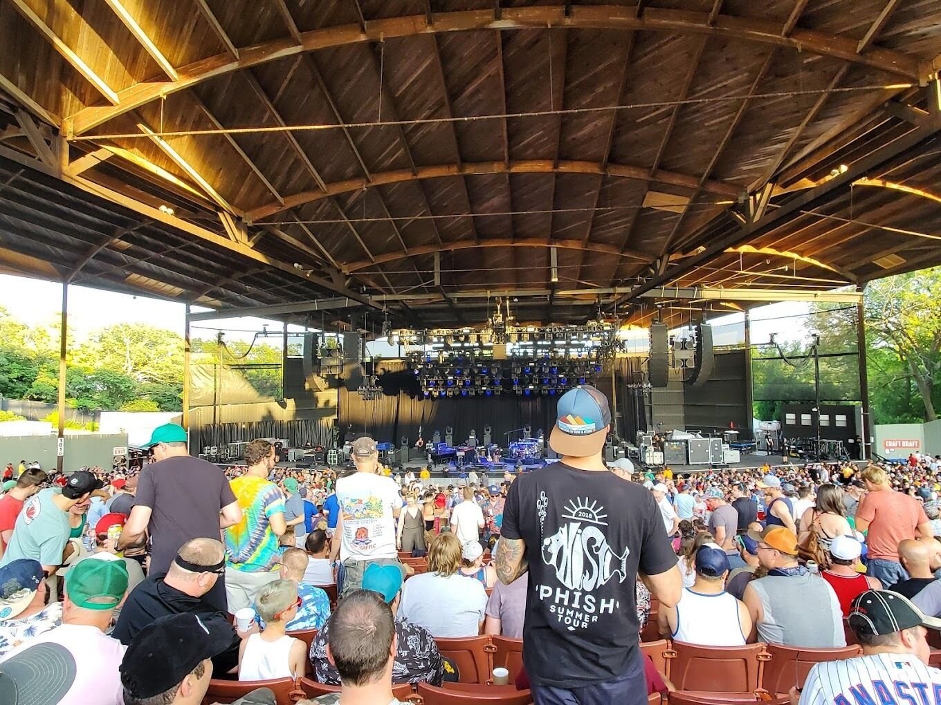 Un recinto cubierto para conciertos al aire libre con asientos escalonados y un escenario frontal.