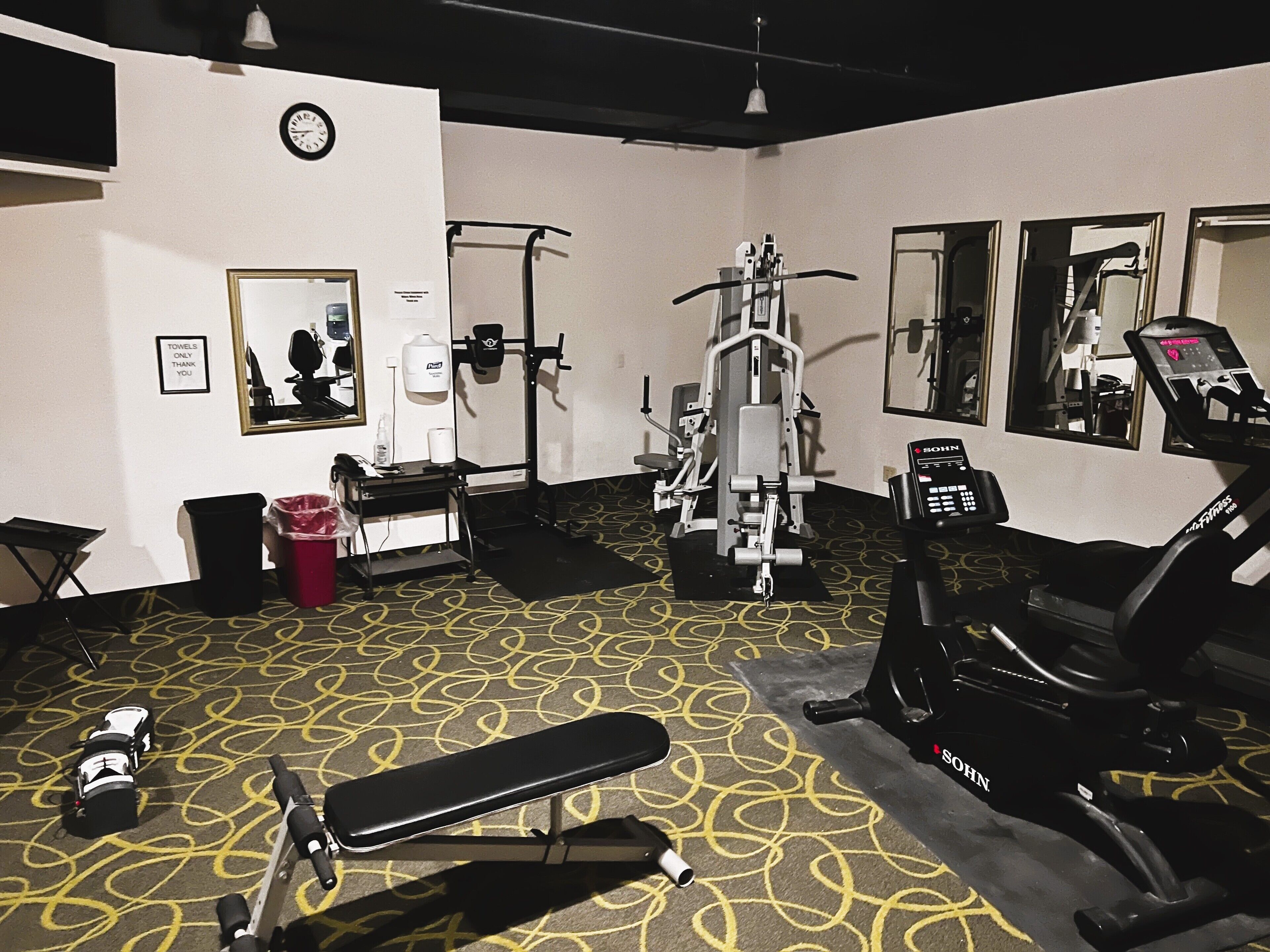 A gym with exercise equipment, a clock, and a mirror.