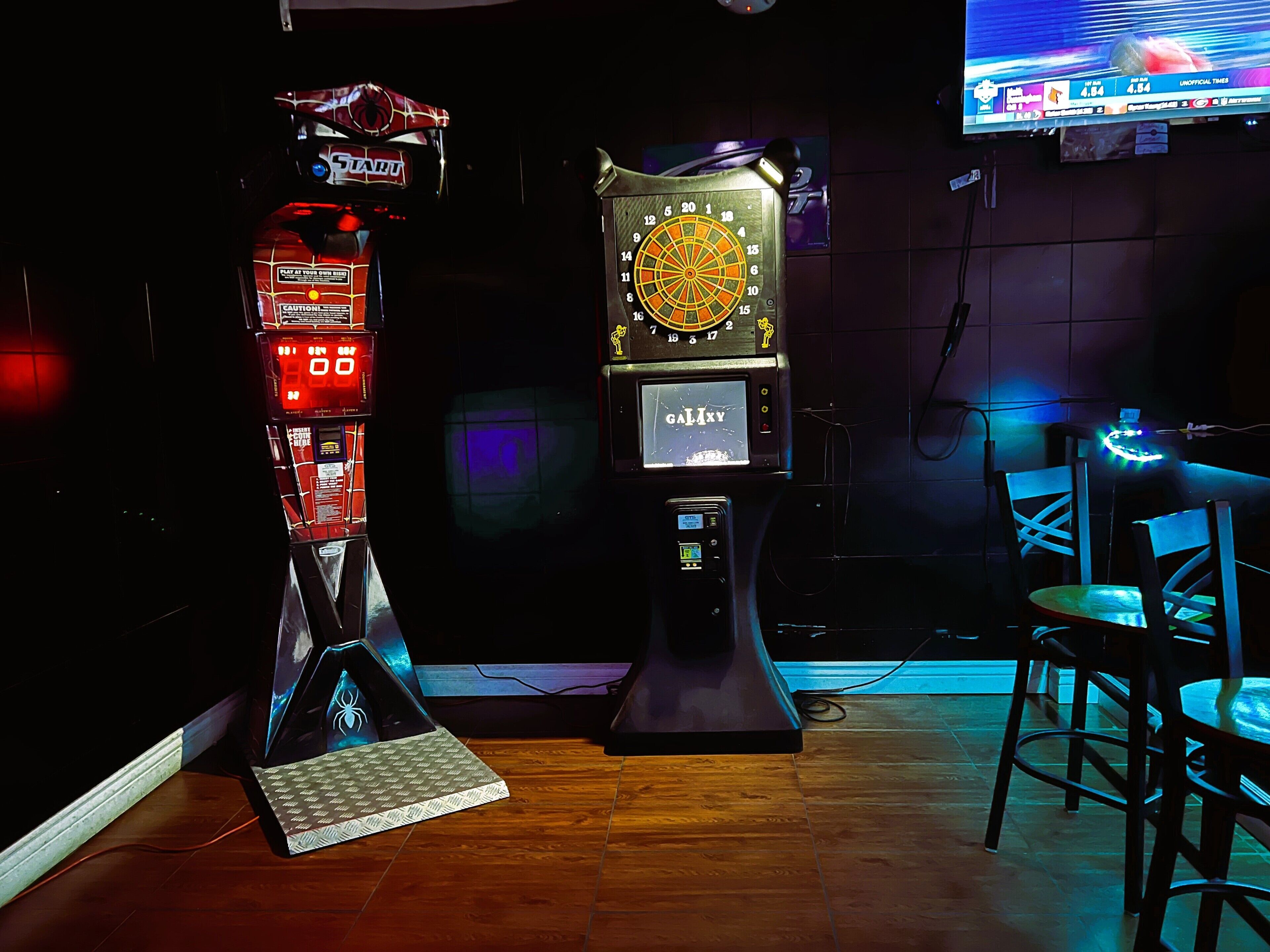 Quarto com dardos, relógio e televisão mostrando esportes.