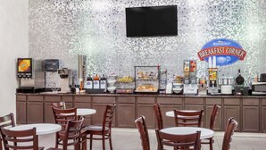 Una barra de desayuno con un letrero de Baymont Breakfast Corner, un televisor montado en la pared y diversos alimentos para el desayuno a la vista.