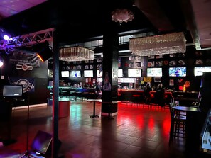 A bar area with multiple screens, bar counters, and seating.