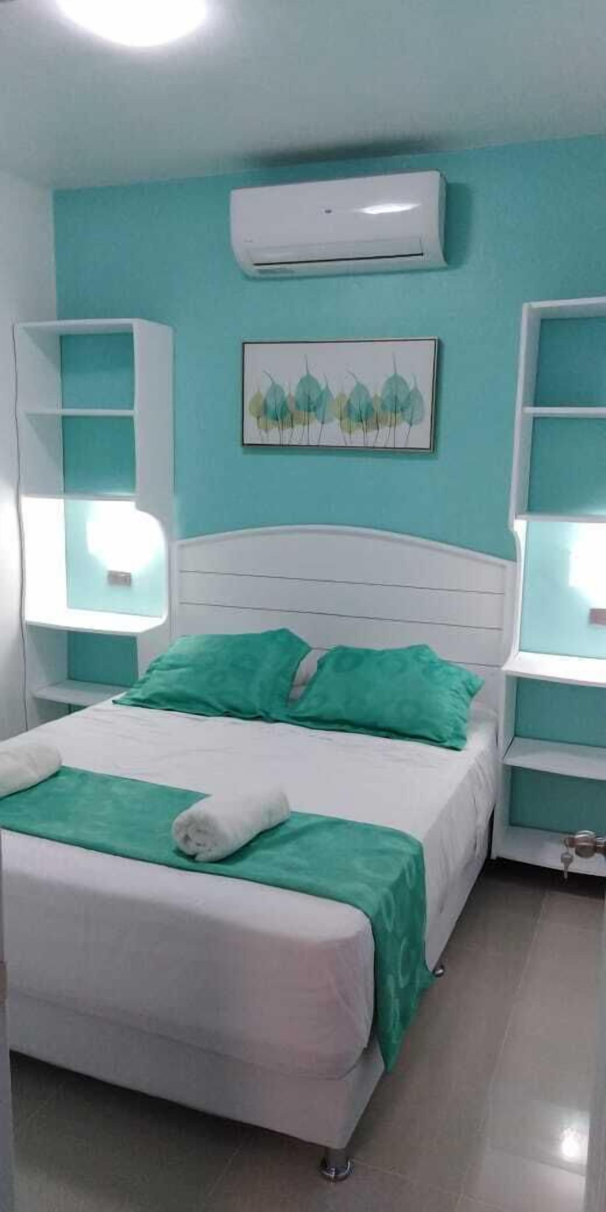 Un dormitorio con una cama, aire acondicionado de pared y dos mesitas de noche con lámparas.