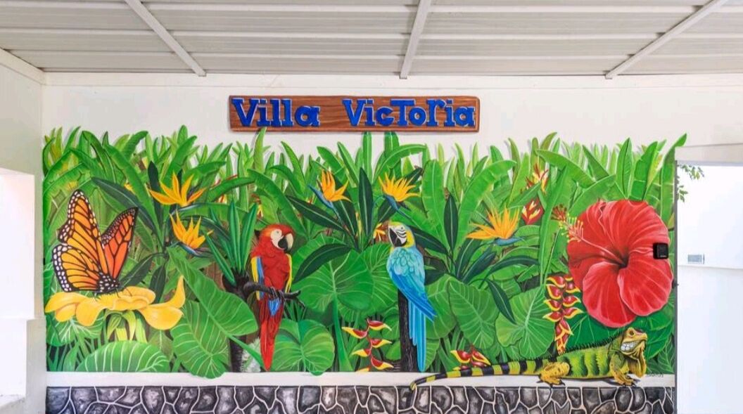 Un murale raffigura fauna tropicale e riporta il testo "Villa Victoria" sulla facciata di un edificio.