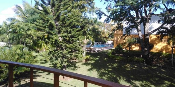 A pool area surrounded by lush greenery and a building with a yellow facade. - Villa Victoria (Sosúa)