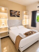 Una habitación de hotel con cama, lámparas de noche, un cuadro en la pared y una ventana con cortinas.