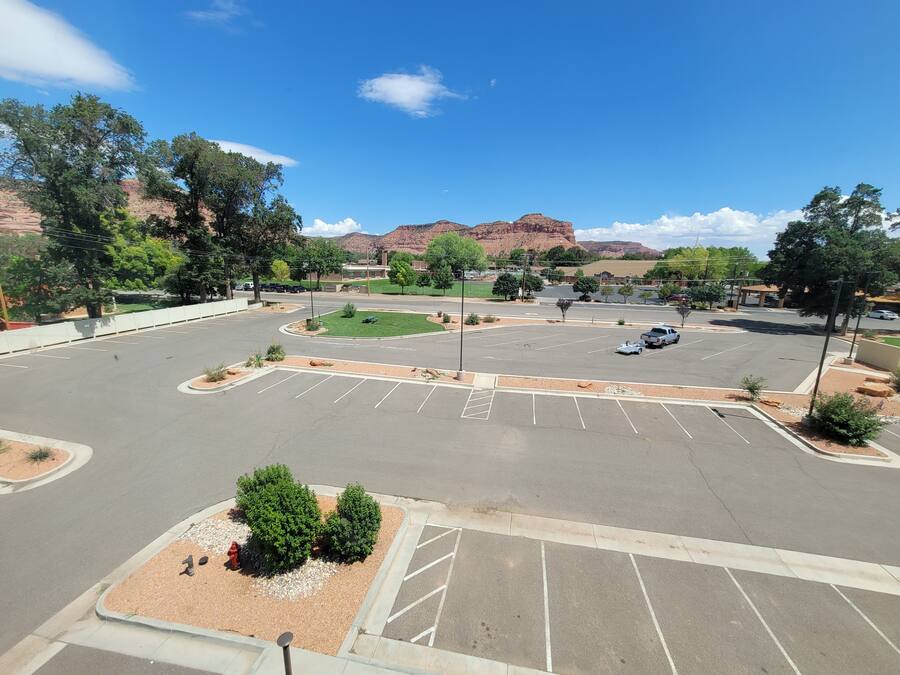 A parking lot with multiple parking spaces, a landscaped area with trees, and a view of mountains in the background.