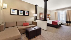 A hotel room with a bed, a sofa, a coffee table, and a desk. There are framed pictures on the wall and a window with curtains. - Comfort Suites Kanab National Park Area (Kanab)