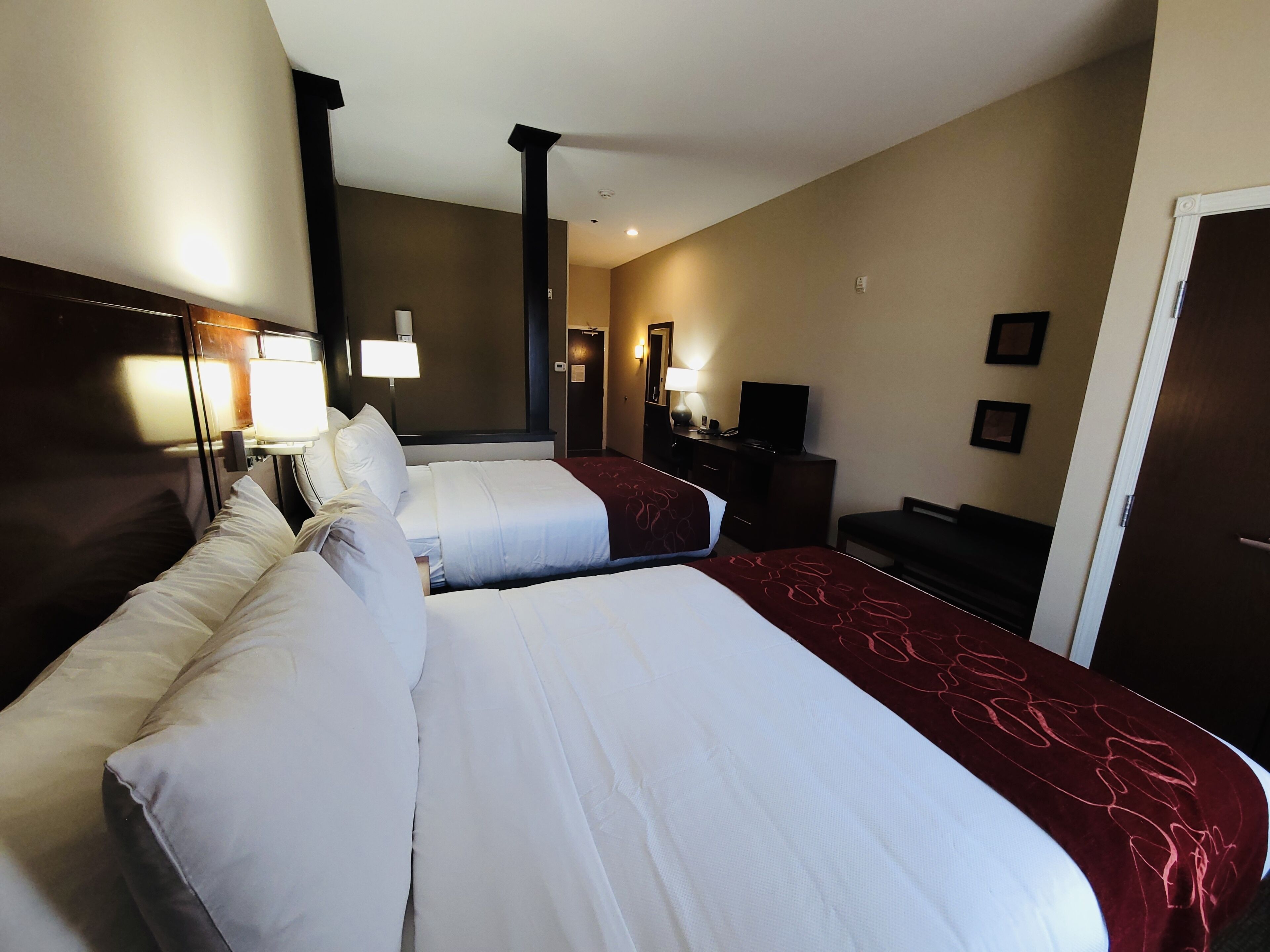 A hotel room with two beds, a desk, a chair, a TV, and a door.