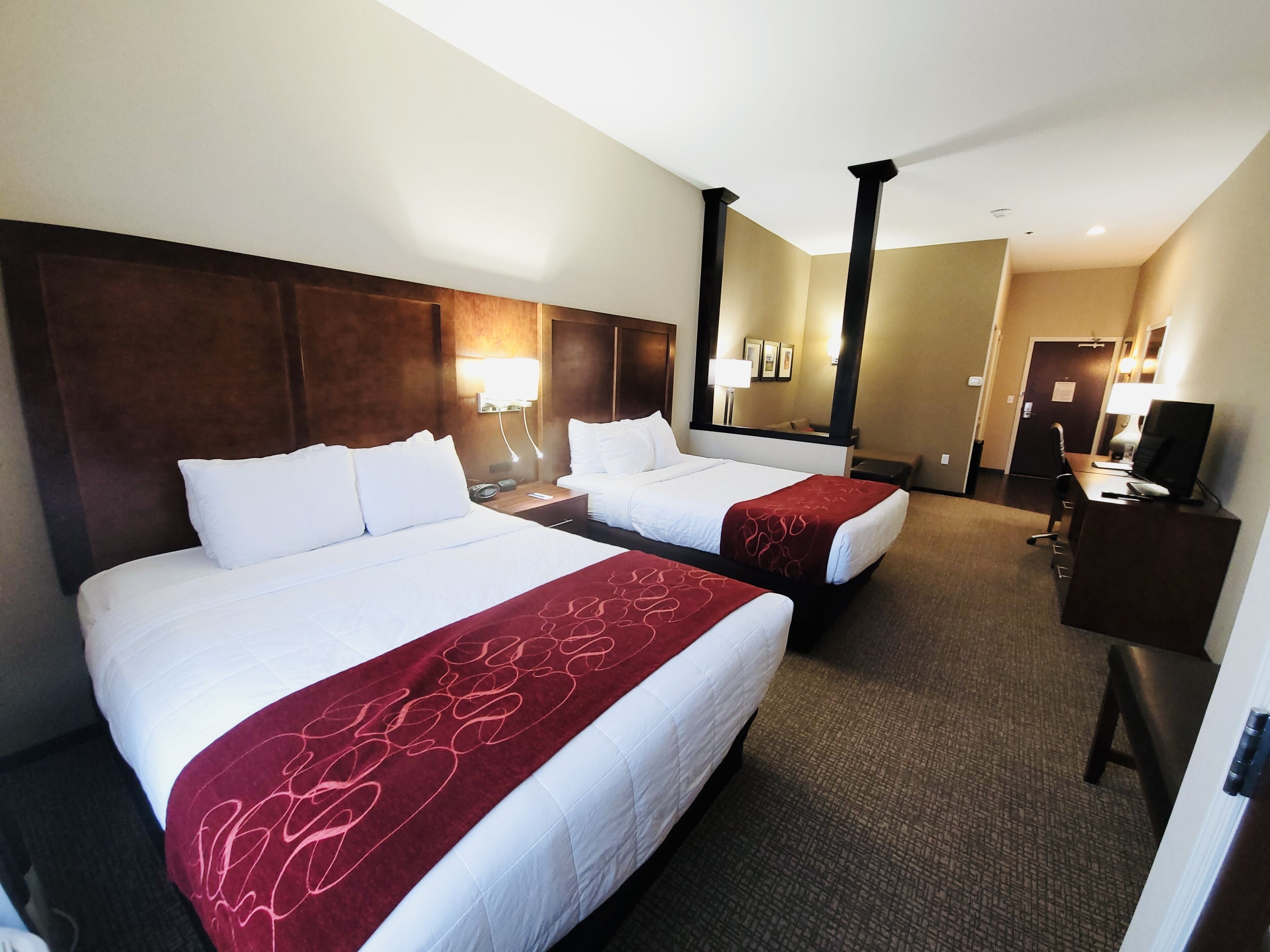 A hotel room with two beds, a desk, a TV, and a mirror.