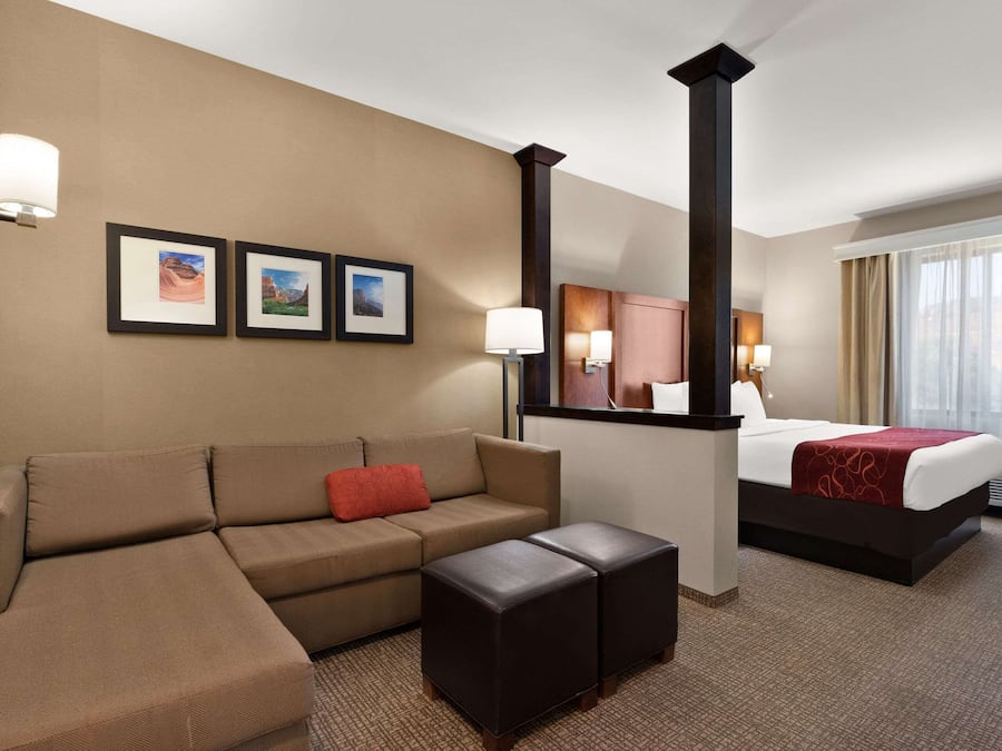 A hotel room with a bed, a sofa, a coffee table, and wall-mounted artwork.