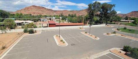 Un estacionamiento con varios espacios, algunos árboles y un edificio de techo rojo al fondo.