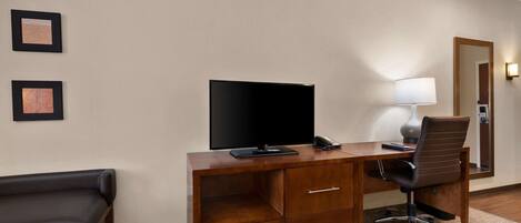 A hotel room with a wooden desk, a flat-screen TV, a lamp, a chair, and a bench.