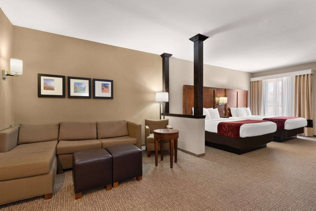 Ein Hotelzimmer mit einer Couch, einem kleinen Tisch, einem Bett mit zwei Kissen und einer Kopfteil. An der Wand hängen drei gerahmte Bilder.