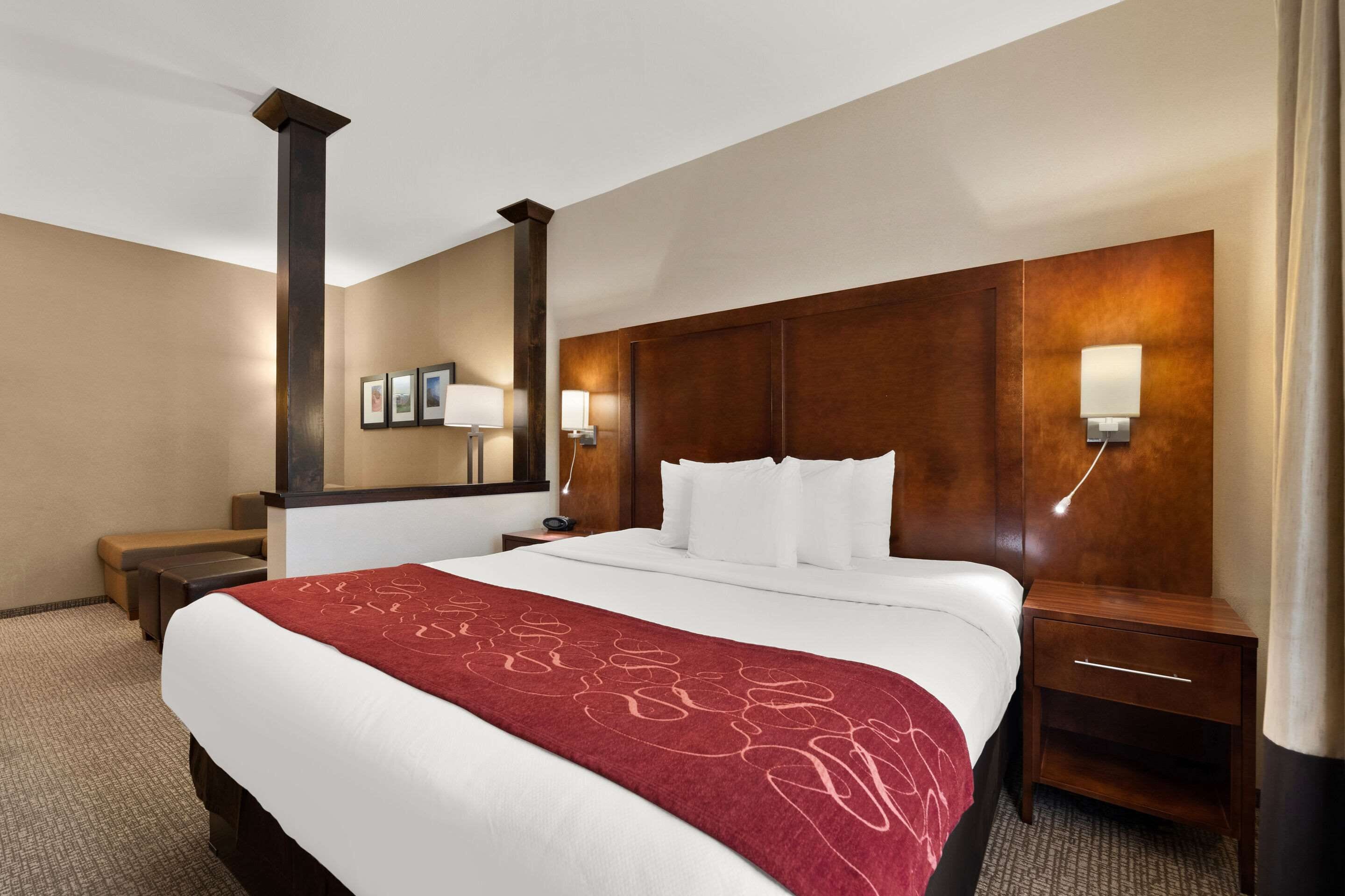 Een hotelkamer met een groot bed, een houten hoofdeinde, een nachtkastje met een lamp en een bankje.