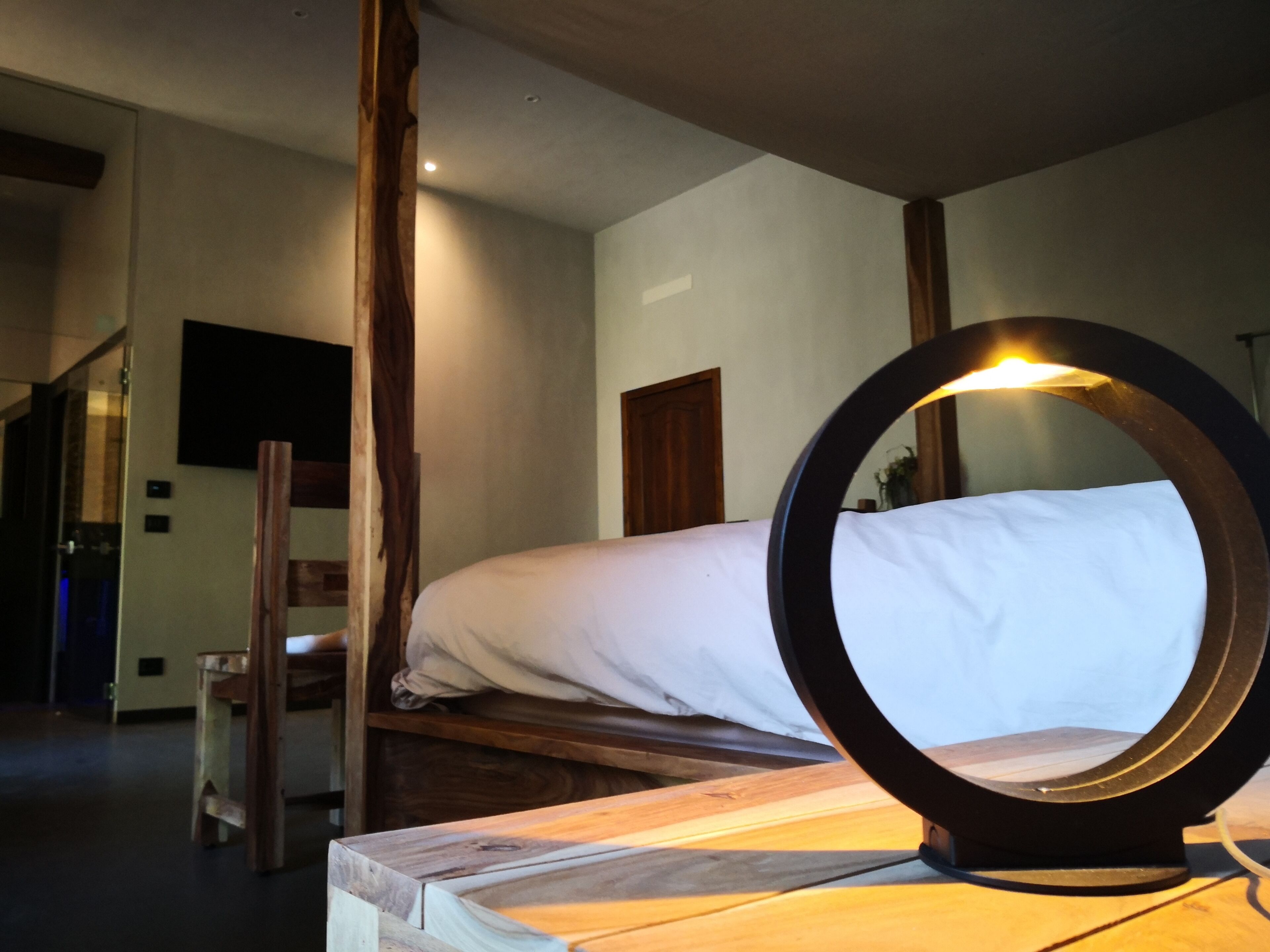 A wooden bed with white bedding, a round mirror on a bedside table, and a wooden chair.