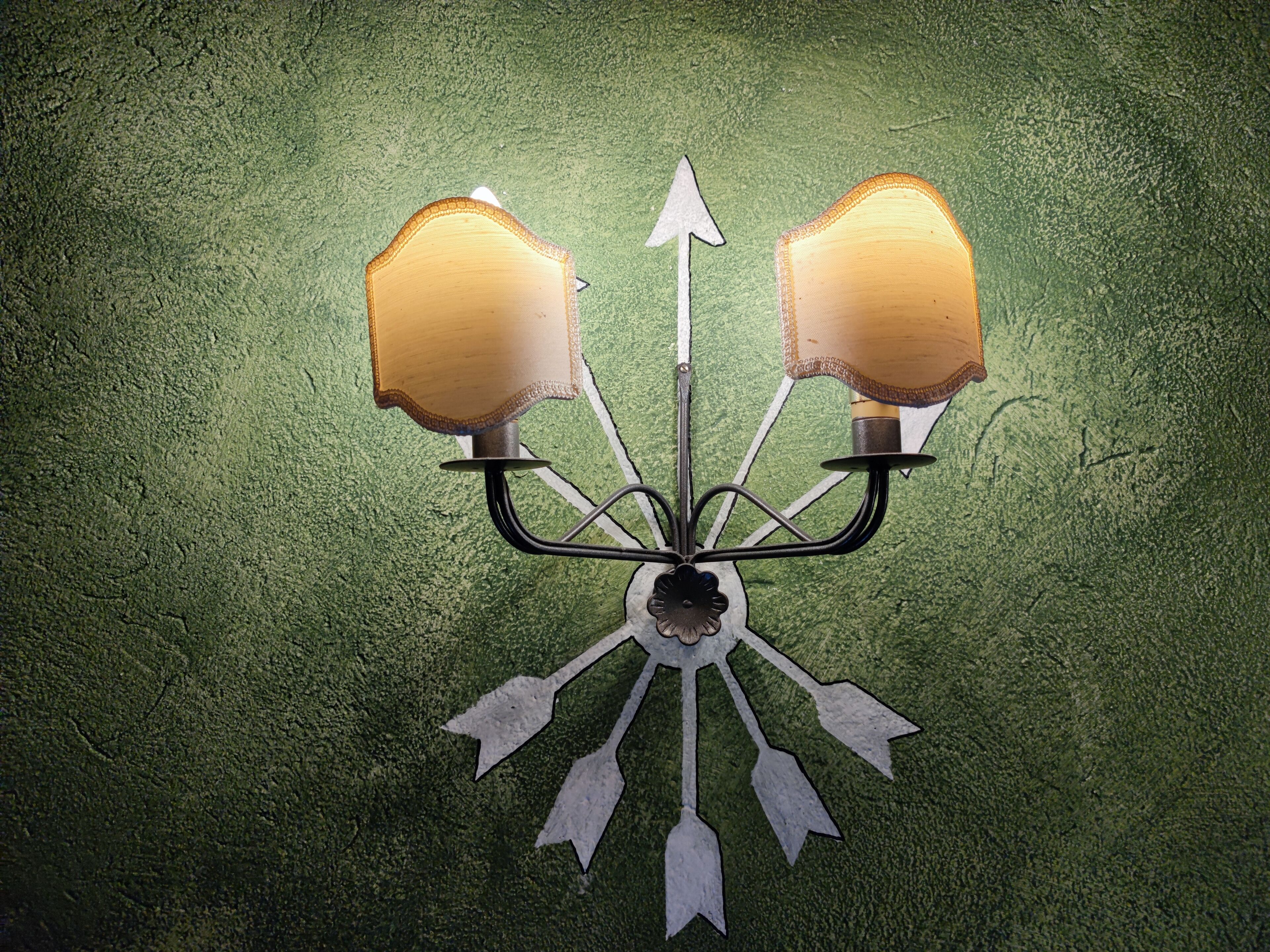 A wall-mounted light fixture with a central bulb and two lamps on either side, connected by metal arms.