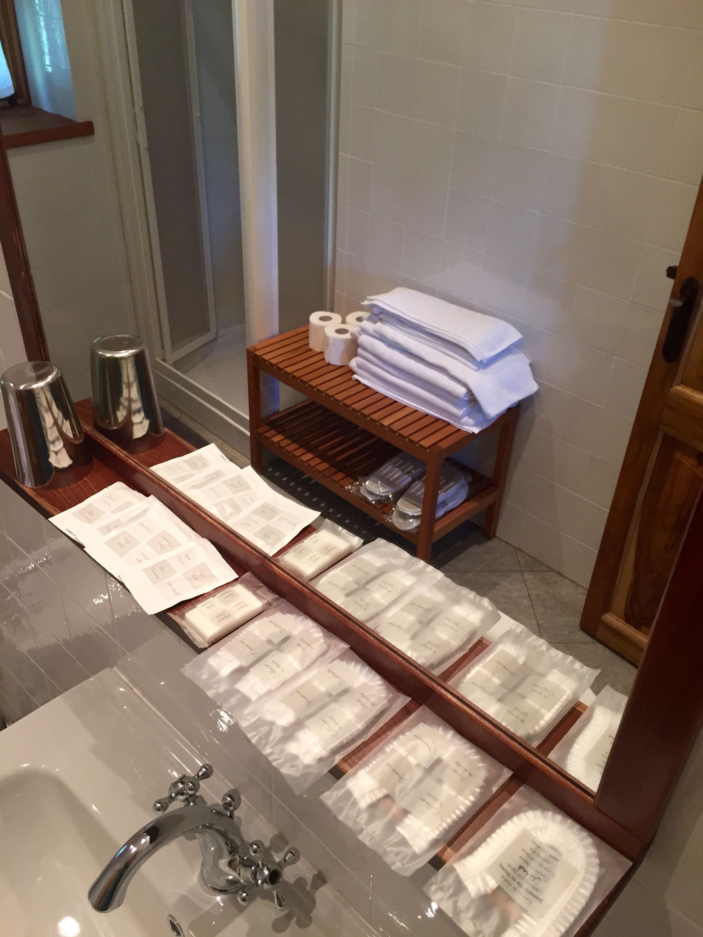 A bathroom with a glass sink, a wooden shelf with toiletries, and a mirror.