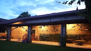 Un edificio rustico in pietra con una veranda coperta, posti a sedere all'aperto e una scala che conduce a un livello superiore.