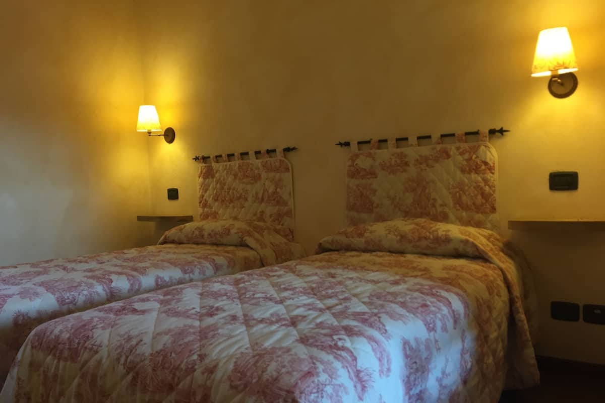 A room with two beds, each with floral-patterned bedding, and two wall-mounted lamps providing warm lighting.