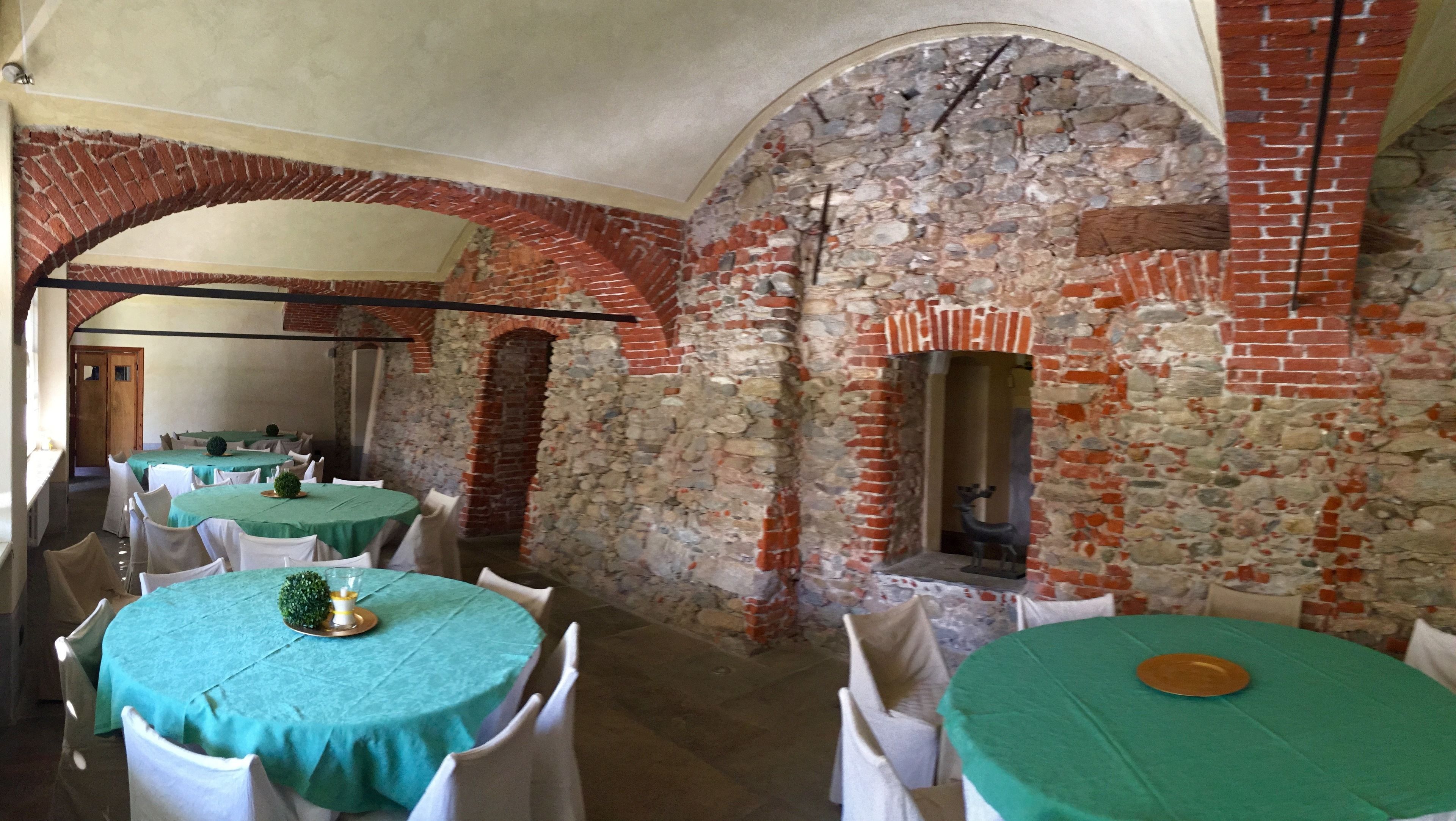 Un comedor con mesas redondas cubiertas con manteles verdes, sillas blancas y paredes de ladrillo con detalles de piedra.